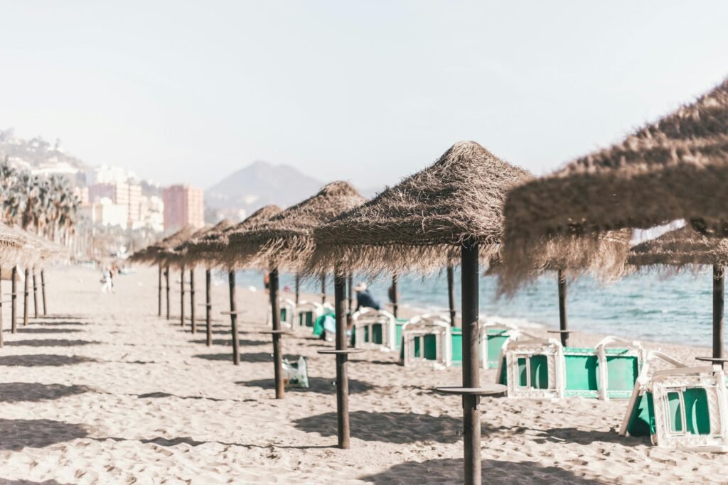 pexels-photo-1884417-1884417 Una tranquila playa de arena con sombrillas de paja y cielos despejados, perfecta para unas vacaciones de verano en Málaga, España.