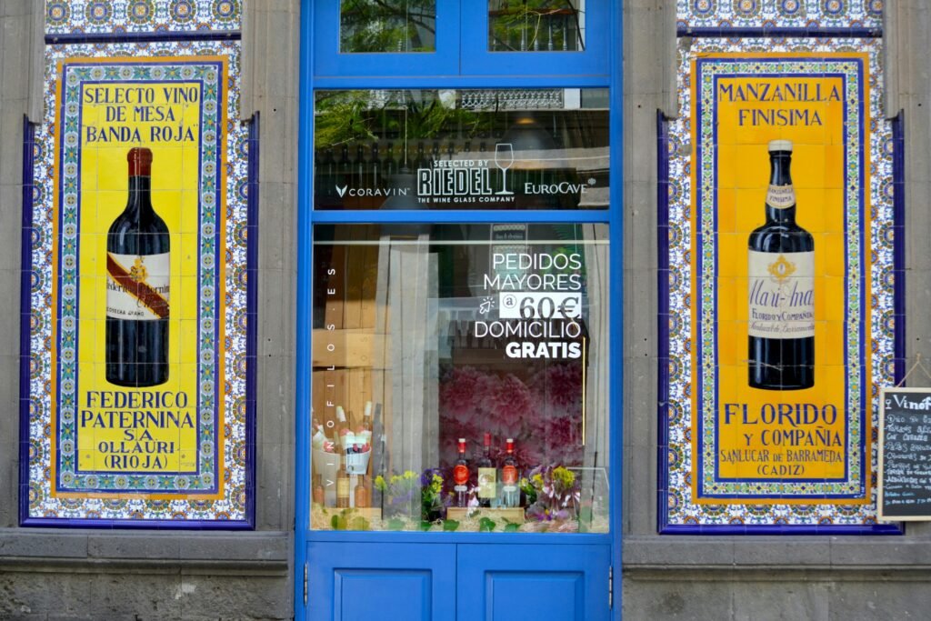 pexels-photo-32802223-32802223 Vibrant shopfront in Cadiz with decorative wine posters and blue entrance.